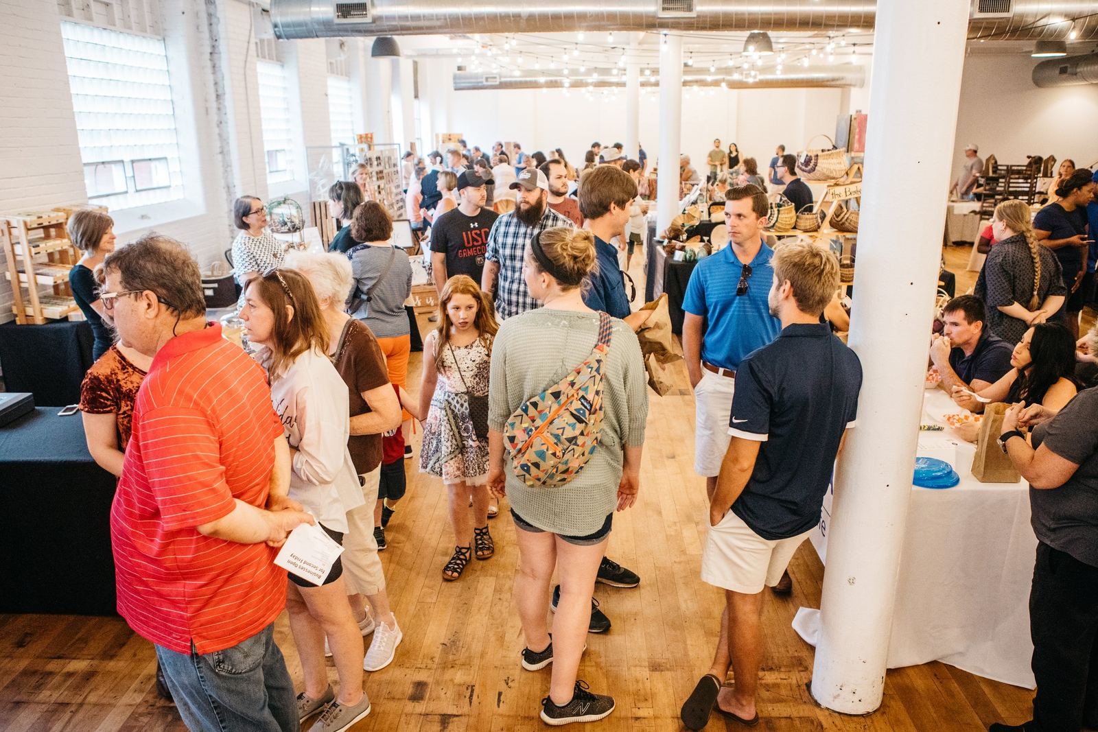 People browsing booths at an indoor craft fair or market with display tables and vendor displays.